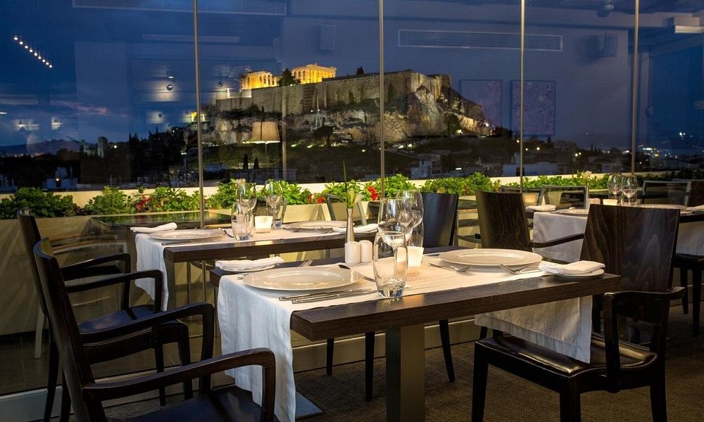 The rooftop restaurant at The Athens Gate Hotel at dusk, the Acropolis lit up beyond