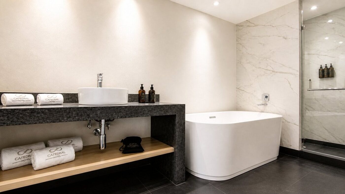 A marble bathroom with a freestanding tub and Hotel Catedral-branded towels