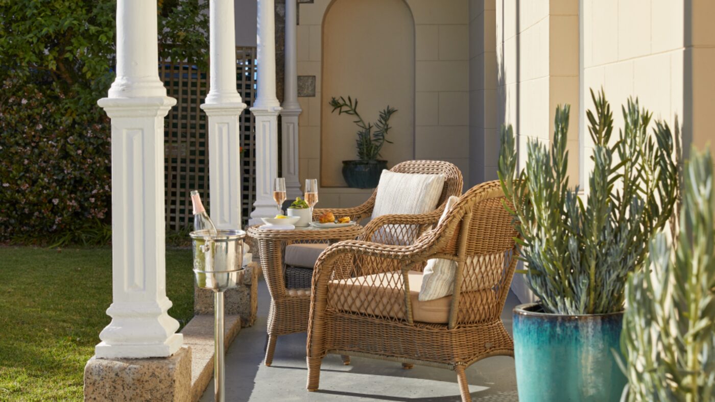 Wicker chairs on a colonnaded porch, set with champagne and canapés