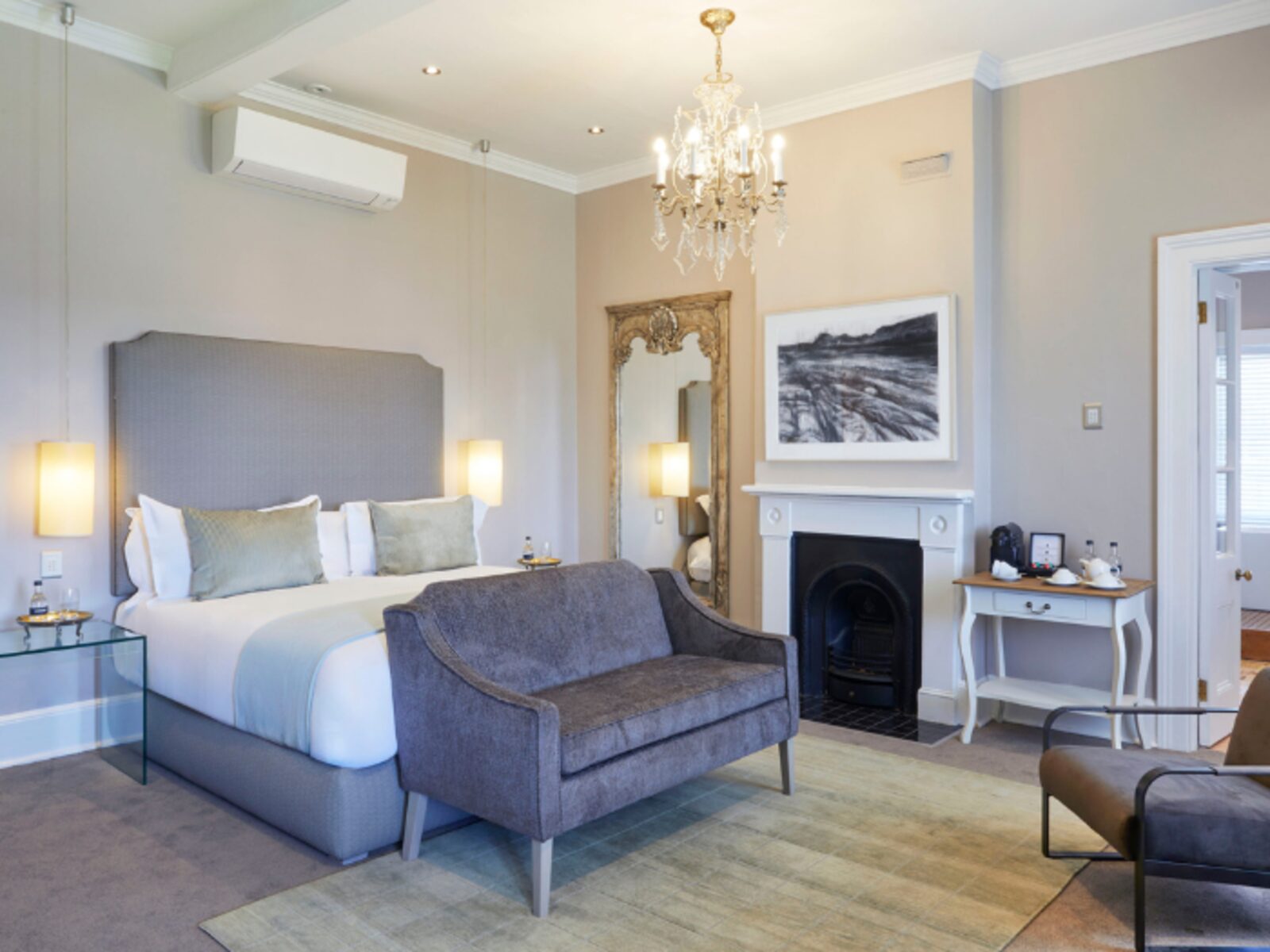 A room at Dock House with a crystal chandelier, upholstered headboard and period fireplace