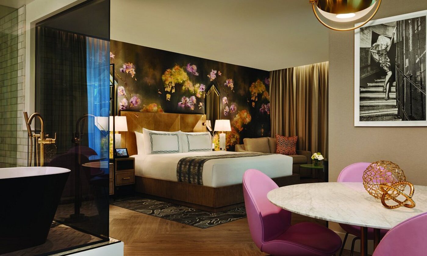 A suite with a floral mural, pink dining chairs and an open bathroom