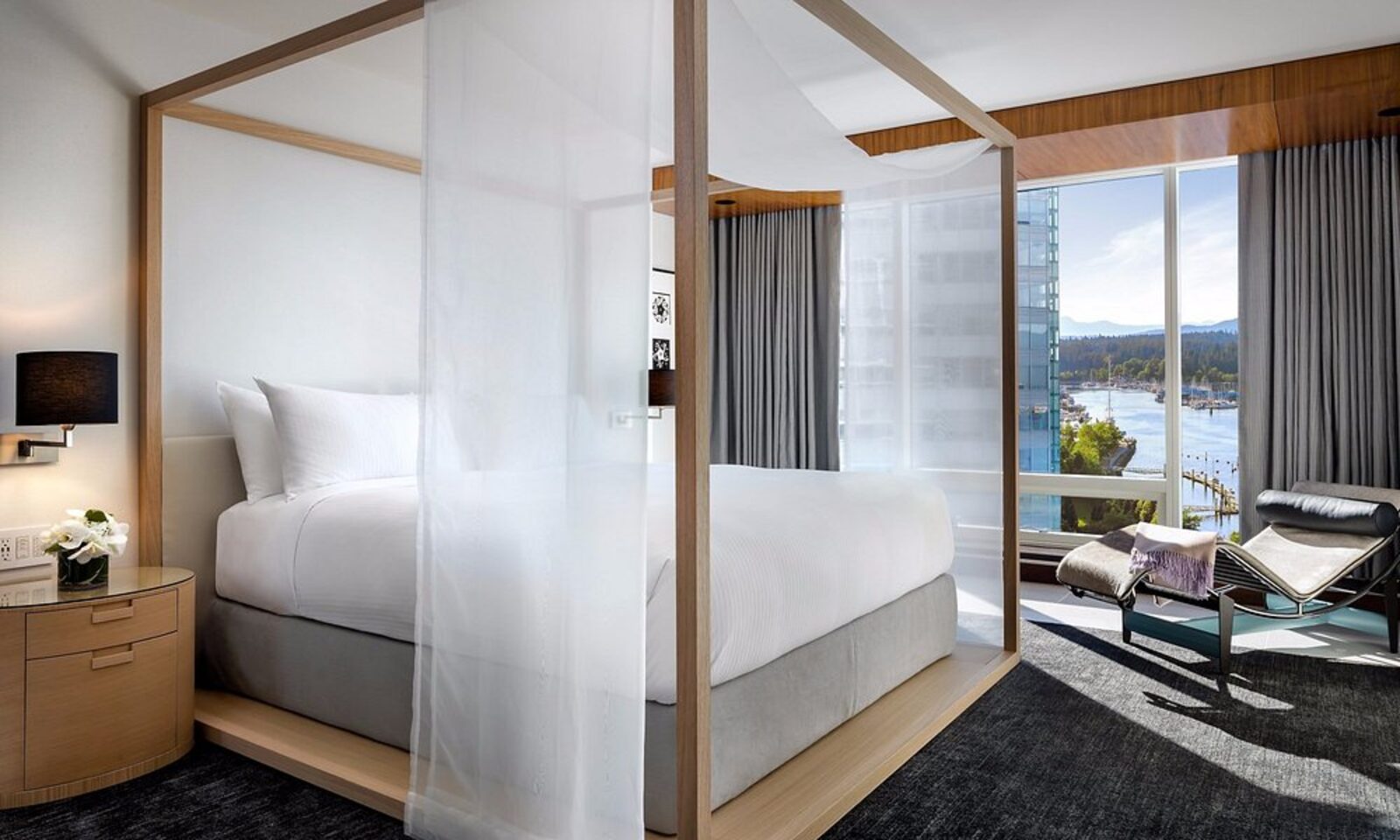 A four-poster canopy bed at Fairmont Pacific Rim, with harbour views through floor-to-ceiling windows