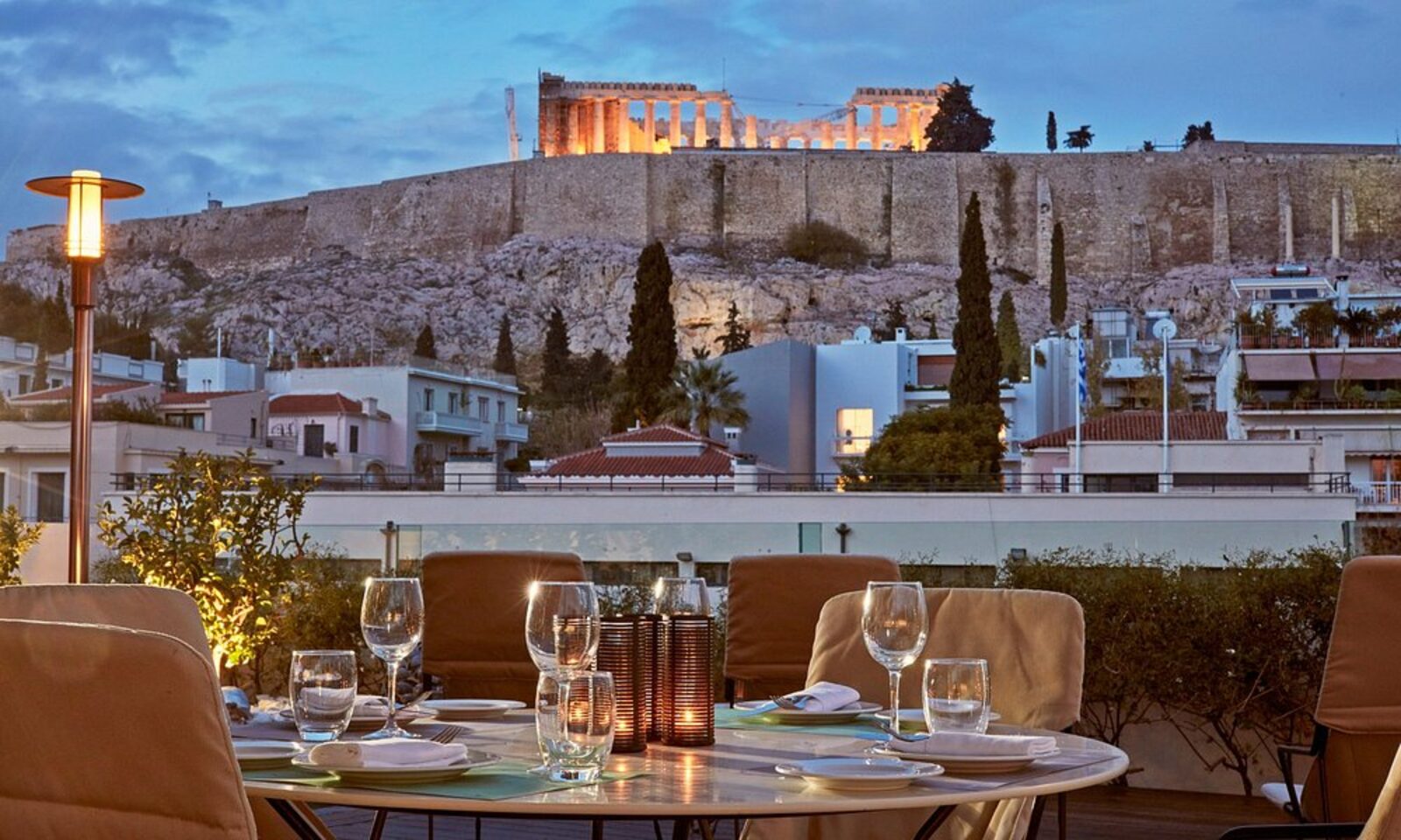 A table set on the rooftop terrace at dusk, with the illuminated Parthenon above