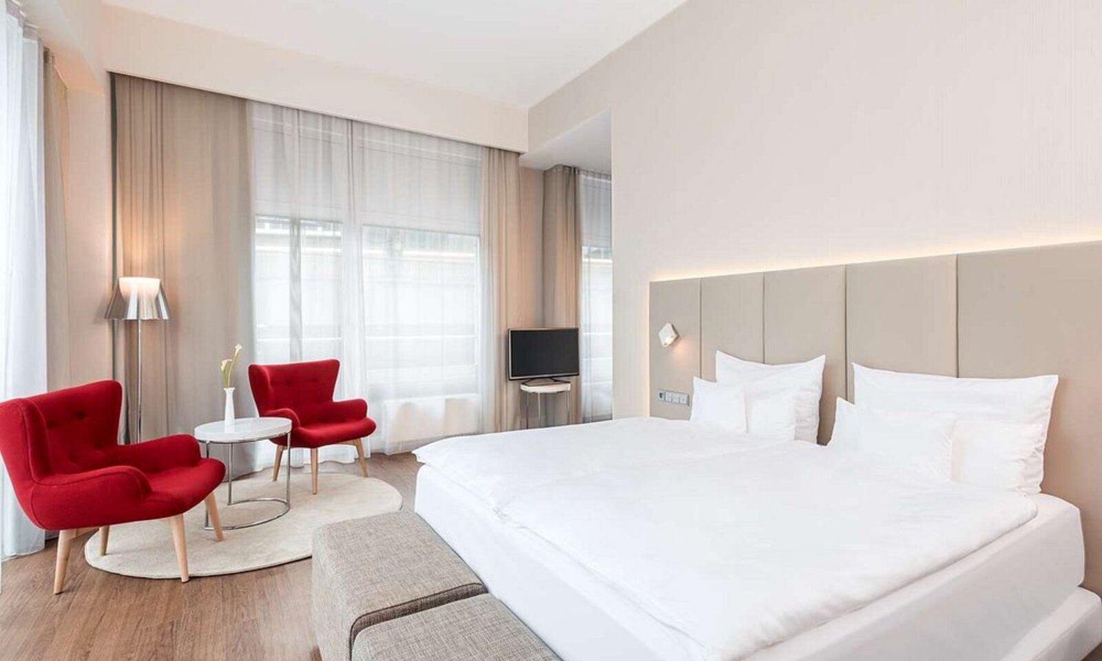A spacious, neutral-toned room at NH Collection Berlin Mitte Friedrichstrasse with red accent chairs