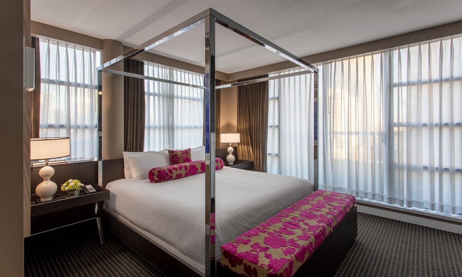 A room at OPUS Vancouver with a canopy bed frame and bold magenta accents