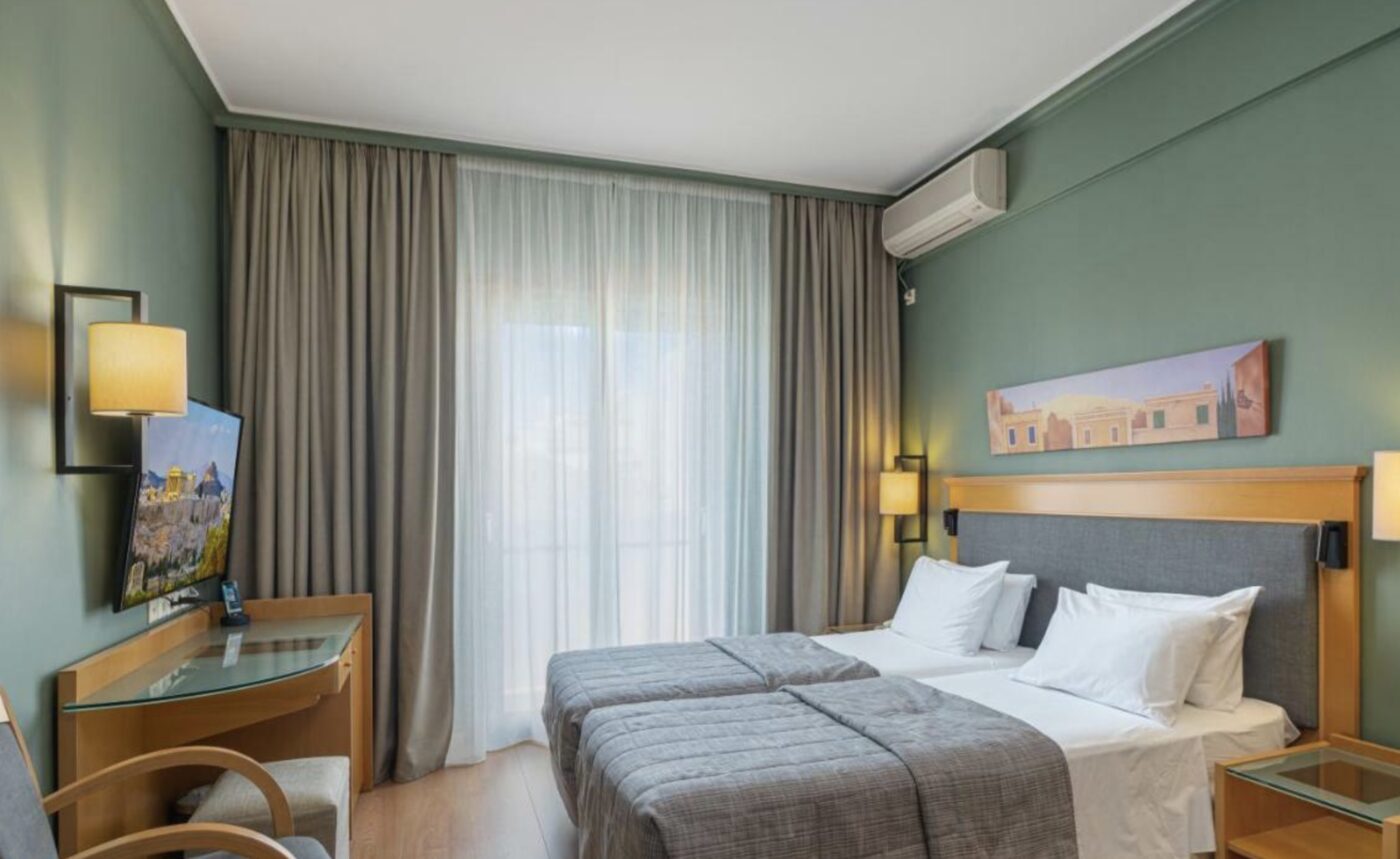 A twin room at Plaka Hotel with sage-green walls and a curtained balcony door