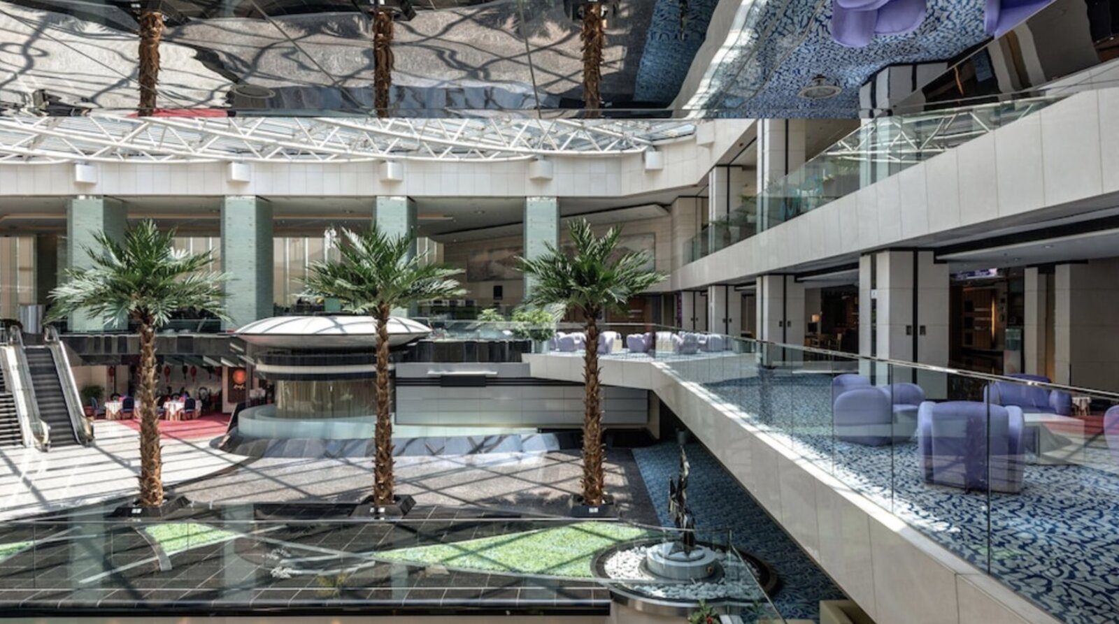 The multi-level atrium lobby at Regal Airport Hotel, with palm trees and escalators