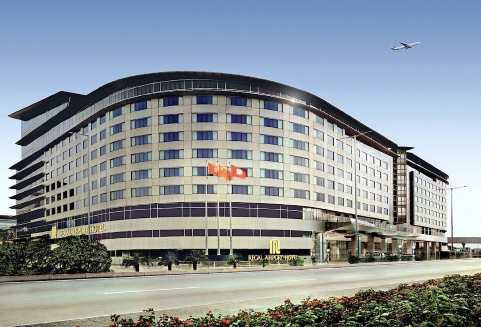 The Regal Airport Hotel's curved facade near Hong Kong International Airport, with a plane taking off overhead