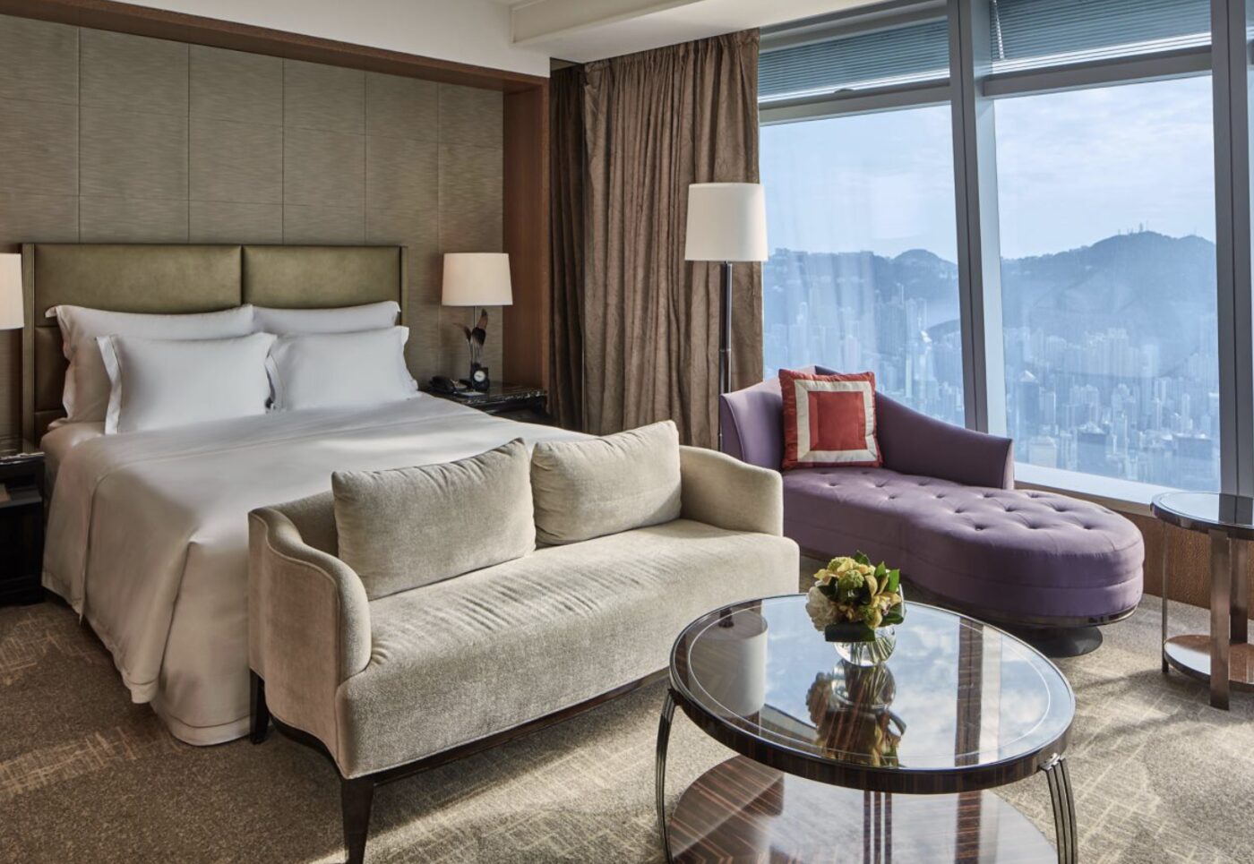 A bedroom seating area at The Ritz-Carlton, Hong Kong with a plum-coloured chaise and city views