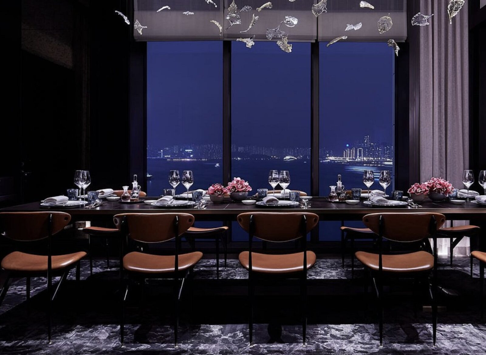 A private dining table set for eight at Rosewood Hong Kong at night, facing the harbour