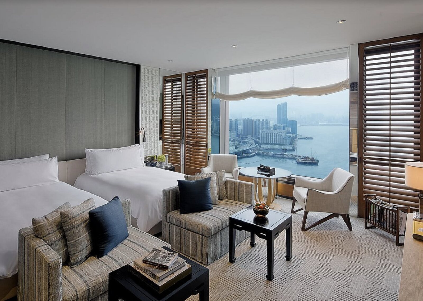 A twin room at Rosewood Hong Kong with a cosy seating nook and harbour view