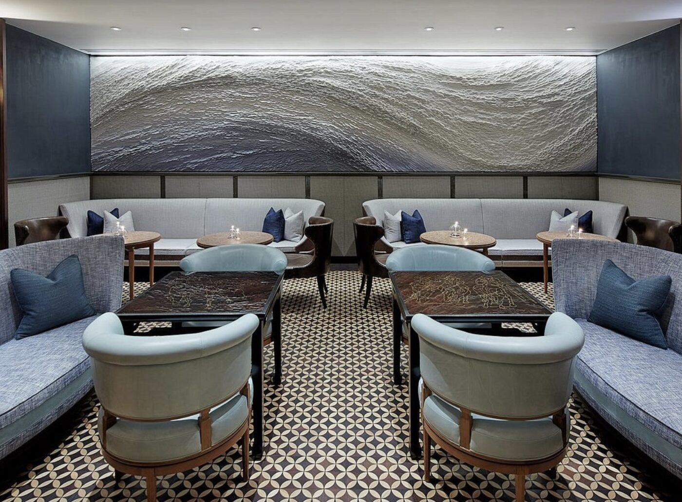 A moody lounge bar at Rosewood Hong Kong with a sculptural wave artwork on the wall