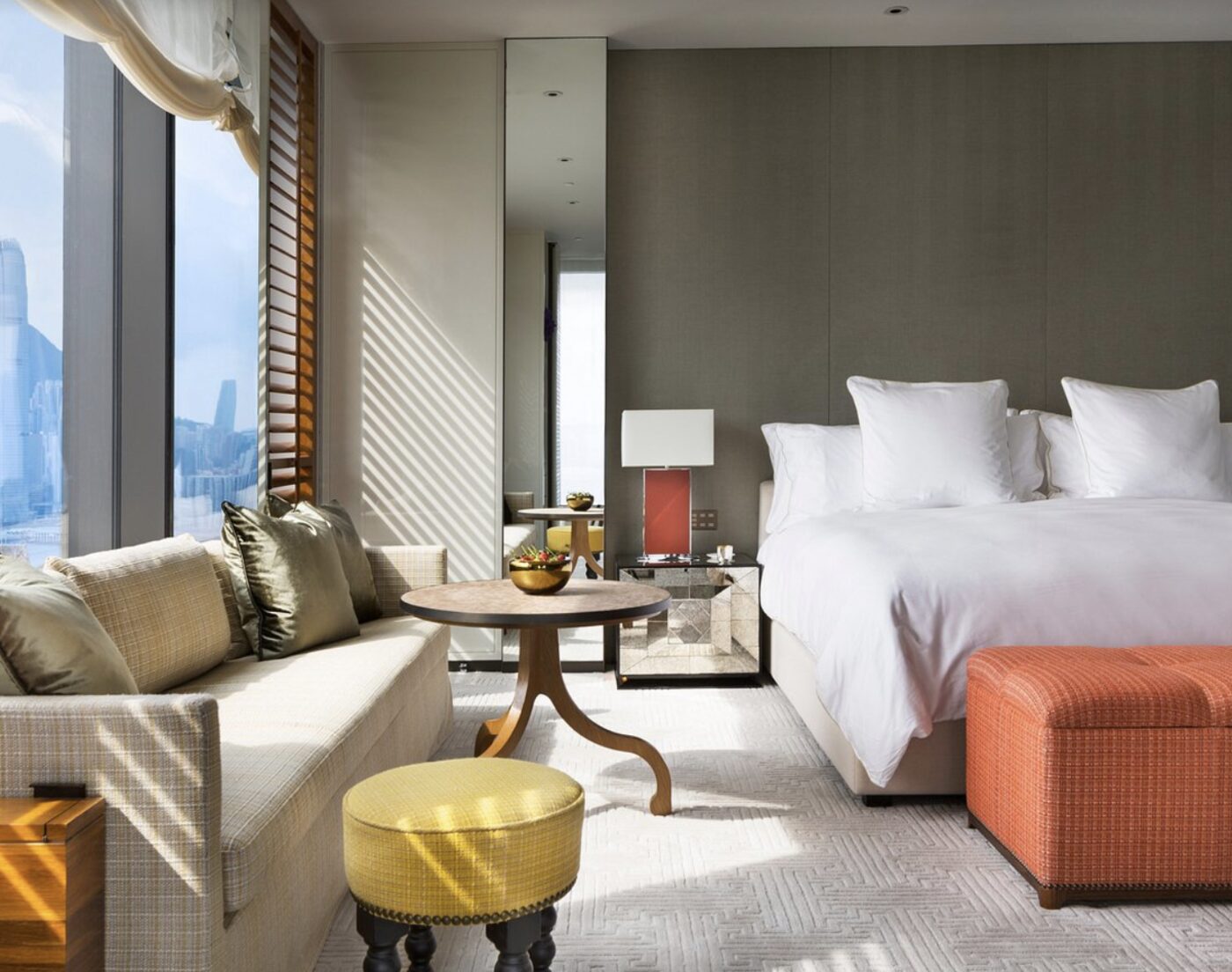 A bedroom at Rosewood Hong Kong with a coral ottoman and a view over the harbour