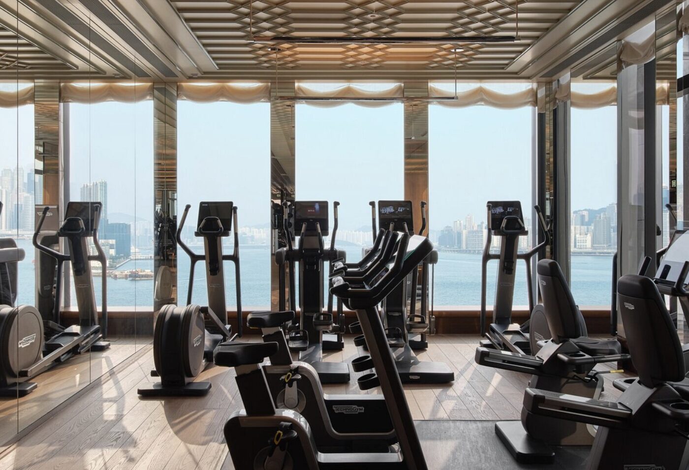 A row of cardio machines at Rosewood Hong Kong facing floor-to-ceiling harbour views