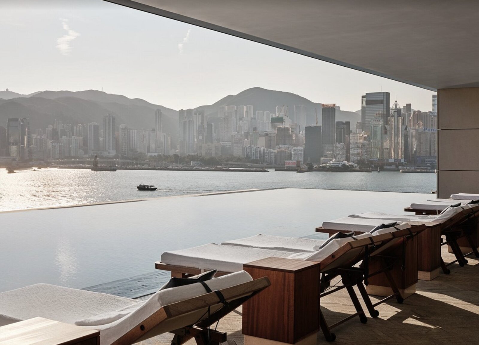 Poolside loungers at Rosewood Hong Kong facing an infinity edge and the Hong Kong Island skyline across the harbour