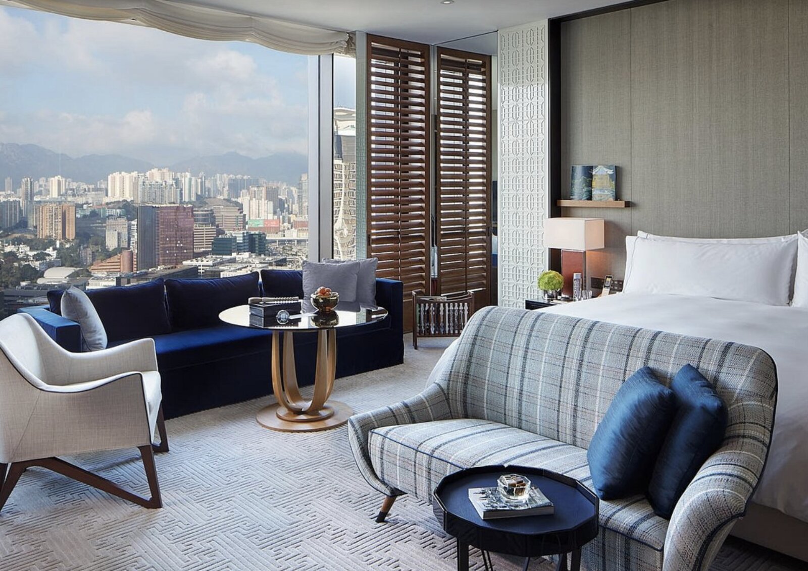 A suite bedroom at Rosewood Hong Kong with a navy velvet sofa and a wide view over Kowloon