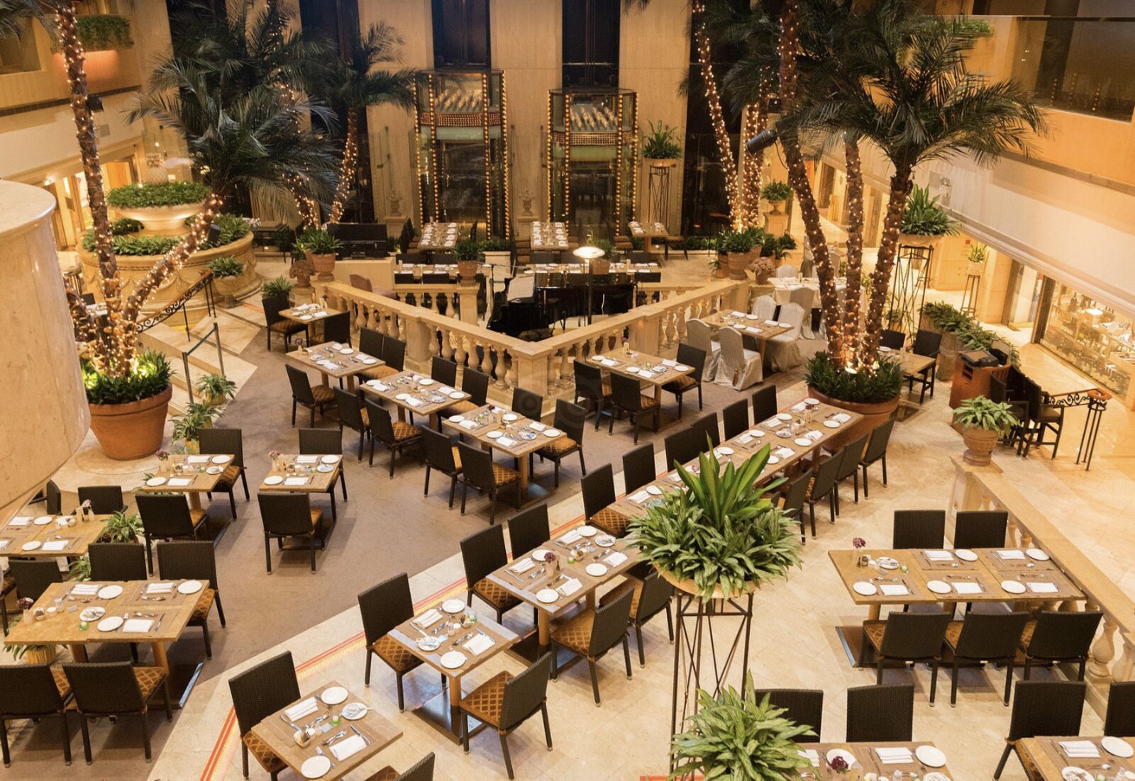 The palm-filled atrium restaurant at The Royal Garden, set for breakfast beneath a grand piano and balustraded terraces