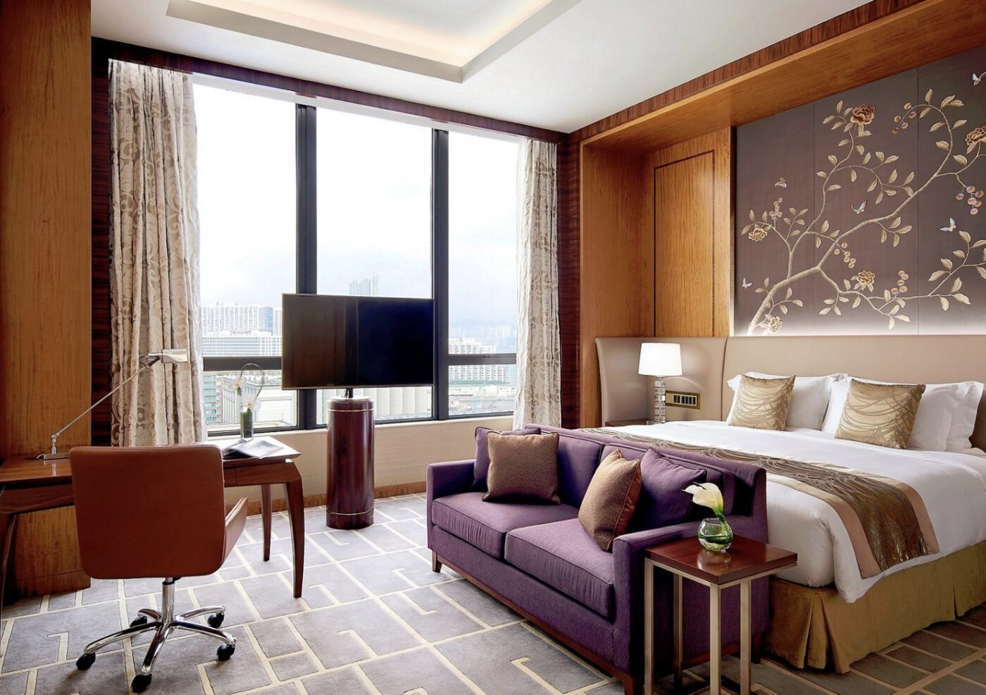 A bedroom at The Royal Garden with a plum sofa and floral wall art above the bed