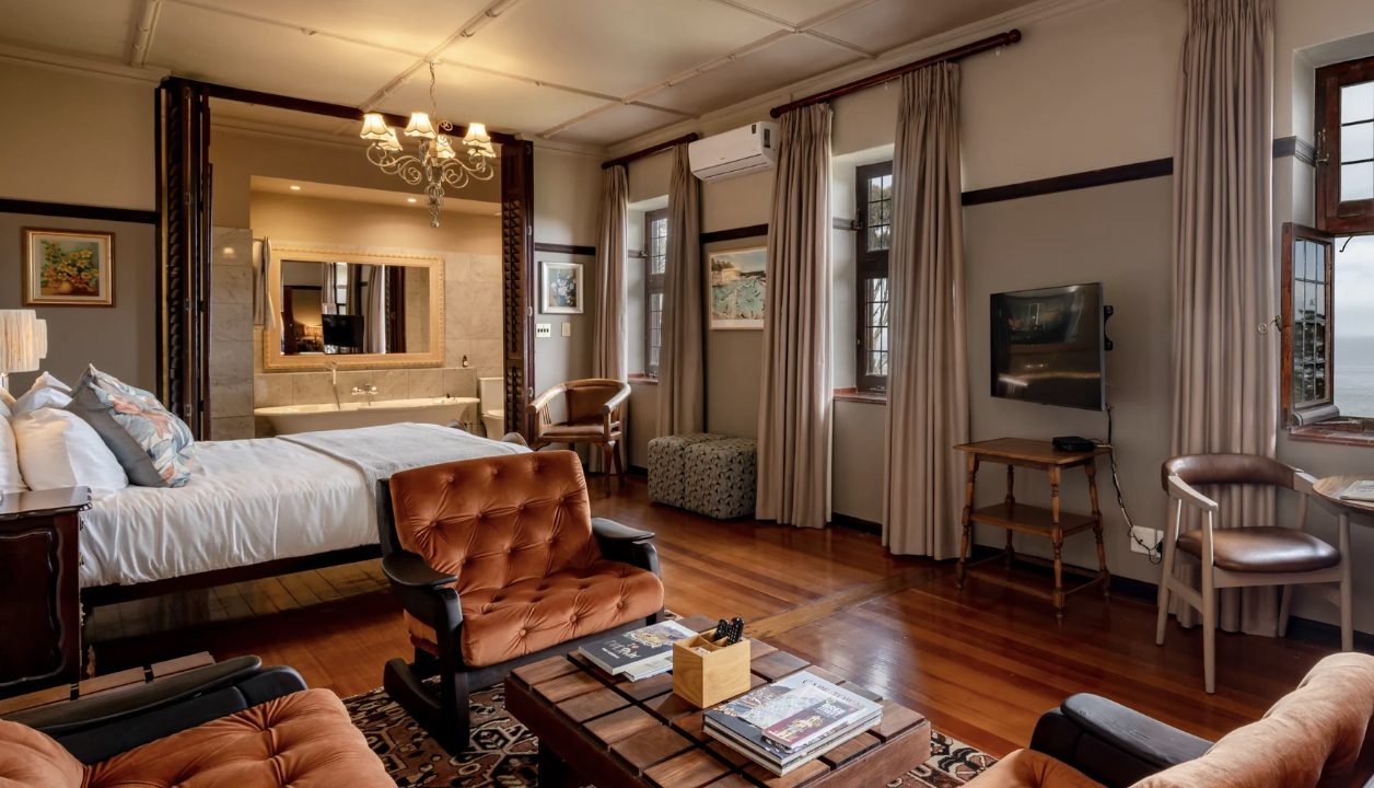 A spacious suite with velvet armchairs, wooden floors and a sea glimpse